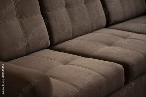 A soft sofa made of brown velour with quilted stitched pillows with a comfortable back and seat. Upholstered furniture close-up with copy space.