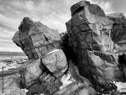 A black-and-white photograph of the Okotoks Erratic, a massive glacial rock formation in Alberta, Canada, surrounded by a snow-dusted field and a cloudy sky. photo