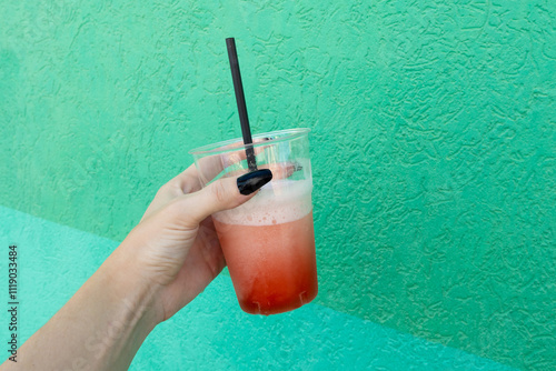 red drink in hand in front of tropical seafoam green blue wall with black nails photo