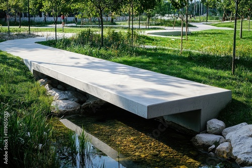 A minimalist concrete footbridge crossing a small, clear creek in a modern park photo