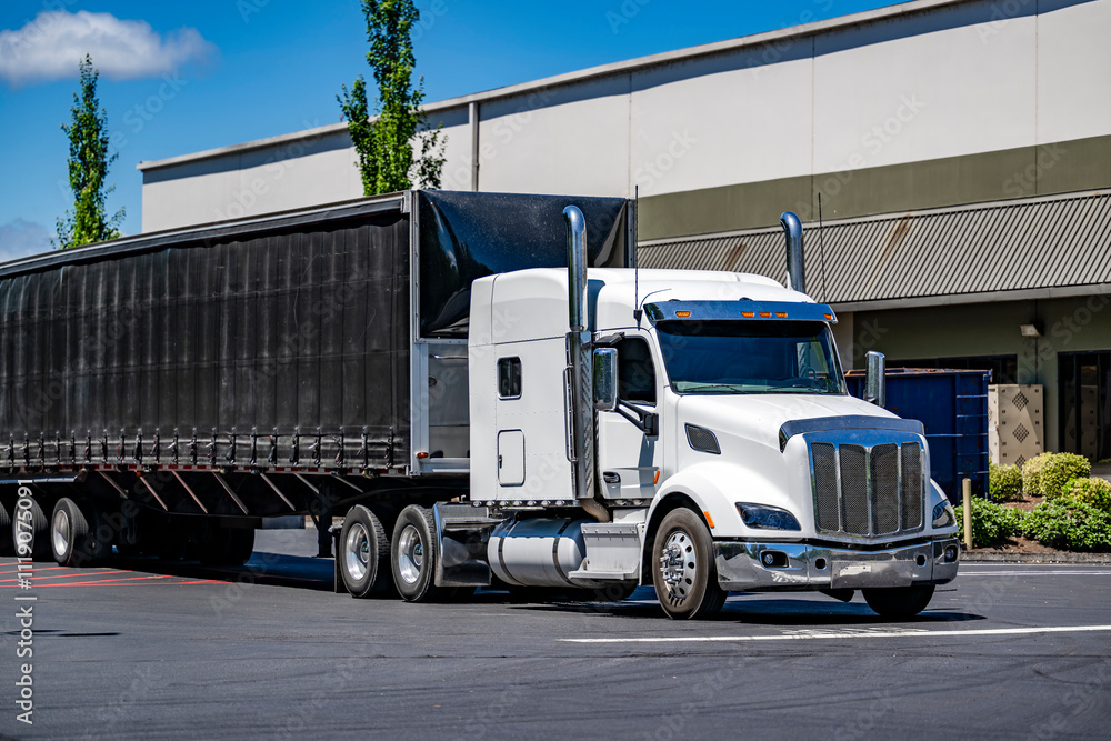 Extended cab white big rig semi truck with conestoga flat bed semi trailer standing on the warehouse parking lot waiting for commercial load Extended cab white big rig semi truck with conestoga flat bed semi trailer standing on the warehouse parking lot waiting for commercial load