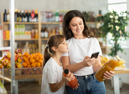 Mother and daughter choose bottles of juice and scan QR code with smartphone photo