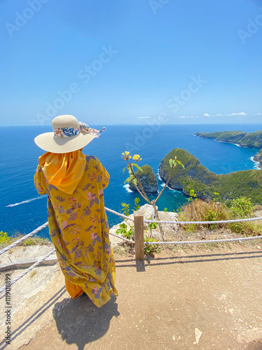 Bali, Indonesia - October 26, 2024: A person is posing on the edge of the Paluang Cliff, with a backdrop of a beautiful view of the blue sea and small islands.
 photo