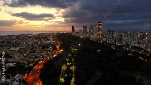 Skyscrapers and buildings along Avenida Anacaona at sunset, Santo Domingo city in Dominican Republic. Aerial backward and urban landscape photo