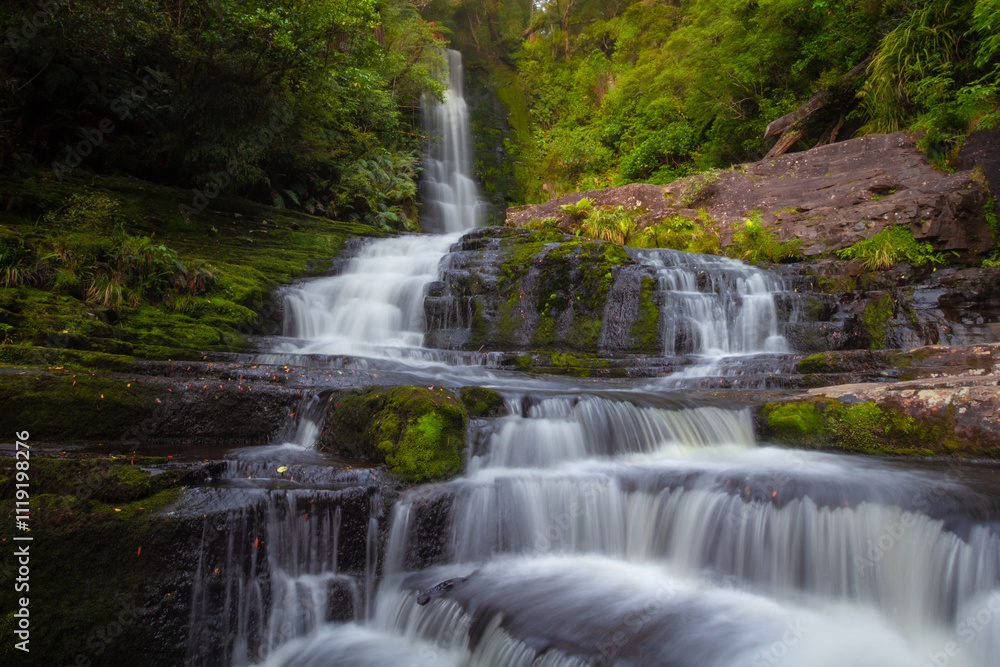 The McLean Falls is located on the Tautuku River in Catlins Conservation Park and have a two-tiered falls that cascades down 22 meters amidst the lush rainforest of Otago New Zealand's South island. The McLean Falls is located on the Tautuku River in Catlins Conservation Park and have a two-tiered falls that cascades down 22 meters amidst the lush rainforest of Otago New Zealand's South island.