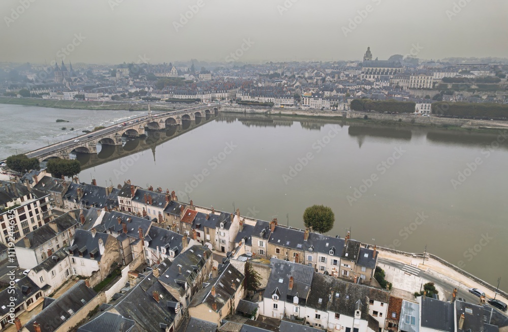 Fototapeta premium Historic town along the riverbank featuring picturesque architecture and a serene bridge on a misty day