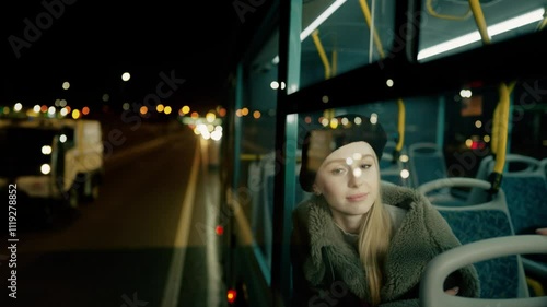 A beautiful young woman looks out the window of a bus going through the night city. 