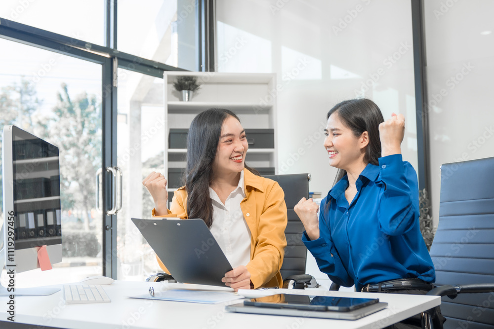 Two Asian businesswomen work on a laptop in an office, pointing at the screen, talking, and smiling with joy as they celebrate positive results of their business success. Two Asian businesswomen work on a laptop in an office, pointing at the screen, talking, and smiling with joy as they celebrate positive results of their business success.