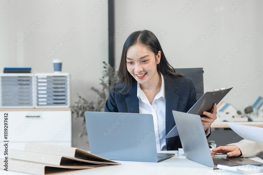 Two Asian businesswomen work on a laptop in an office, pointing at the screen, talking, and smiling with joy as they celebrate positive results of their business success. Two Asian businesswomen work on a laptop in an office, pointing at the screen, talking, and smiling with joy as they celebrate positive results of their business success.