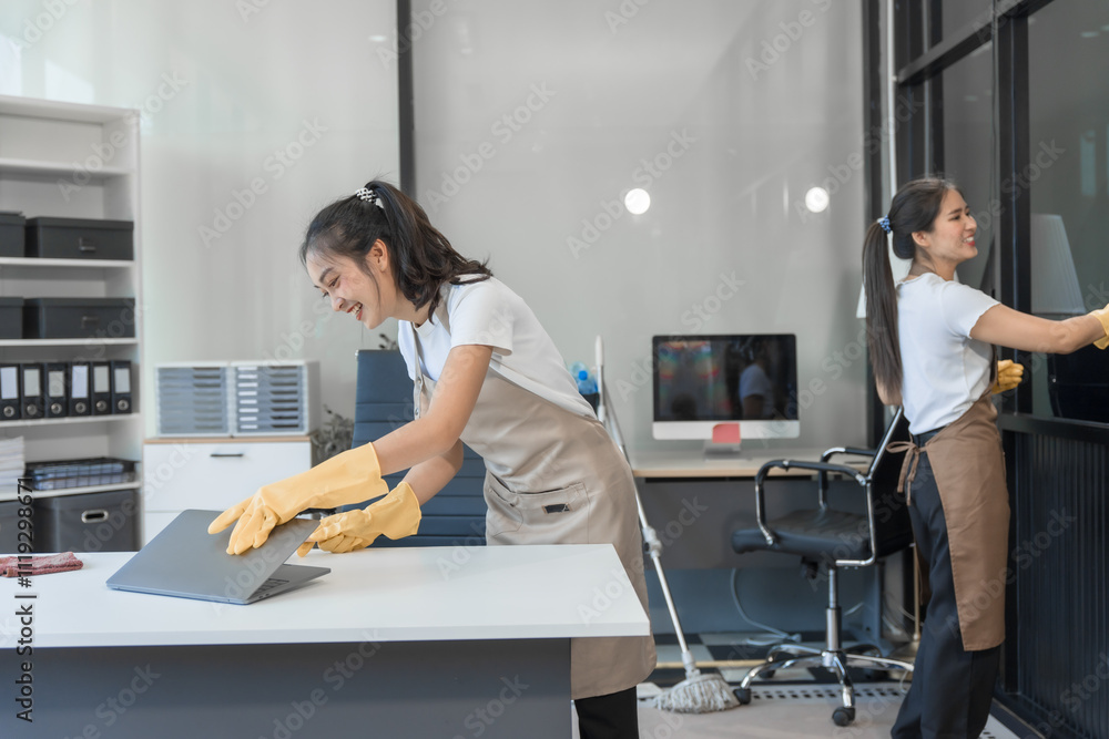 Obraz premium Two Asian housekeepers wear overalls and work together efficiently to clean the living room, study, office.They wipe the windows, mop the floors, inspect the shop to make sure the work is spotless