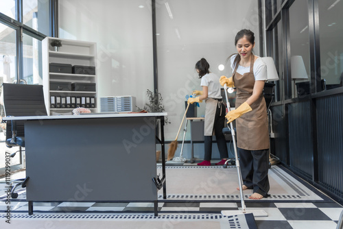 Two Asian housekeepers wear overalls and work together efficiently to clean the living room, study, office.They wipe the windows, mop the floors, inspect the shop to make sure the work is spotless photo