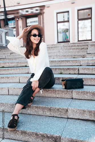 Portrait of young beautiful smiling hipster woman in trendy summer white blouse and jeans. Carefree woman posing in the street in sunny day. Positive model outdoors. Cheerful and happy