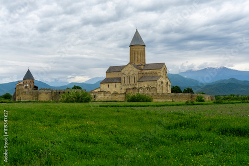 General view of the fortress wall, bell tower, residential buildings, St. George Church of Alaverdi Monastery. Green field, cloudy sky. Caucasus Range in the background photo