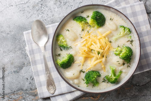 Spicy creamy broccoli gnocchi soup with cheddar cheese, thyme, onion and garlic close-up in a plate on the table. Horizontal top view from above