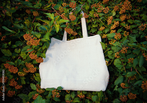 White canvas tote bag mockup template with long handles among the green plant leaves outdoor photo