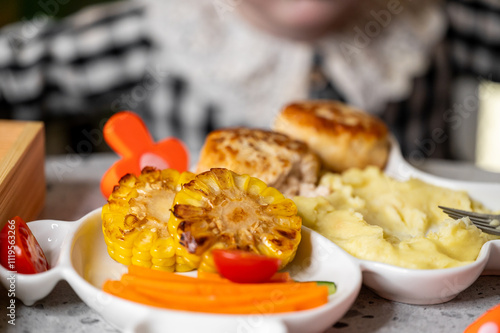 Quadro su tela A beautifully arranged plate featuring grilled corn, mashed potatoes, and carrots, complemented by a small tomato