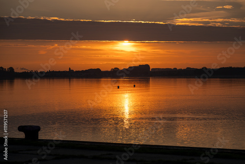 Die Sonne durchbricht mit rotem Licht die Wolken und spiegelt sich im Wasser photo