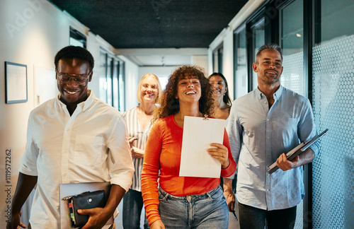 Diverse Team Walking Down Hallway in Modern Office Environment. They are all carrying some office supplies while smiling and laughing together. photo