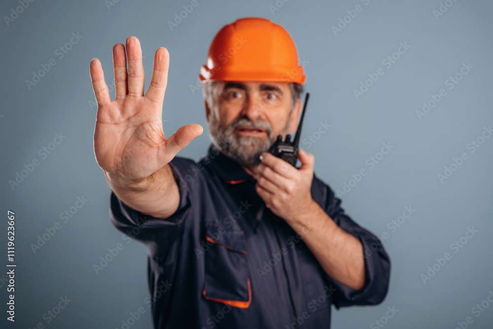 Worker is talking by walkie talkie. Senior man is standing in the studio against background Worker is talking by walkie talkie. Senior man is standing in the studio against background