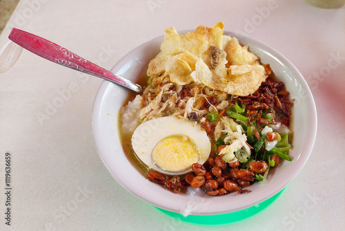 Bubur Ayam, a traditional Indonesian food consisting of white rice porridge, shredded chicken, cakwe, fried soybeans, crackers, green onions and eggs. photo