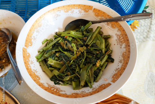 Stir-fried kale vegetables in a white bowl with a rice field background