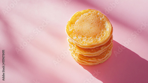 Fluffy pancake stack on a pastel pink background with soft shadows creating an inviting and warm atmosphere