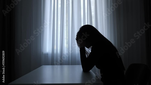 Silhouette of woman sitting at table in front of window. lays head on desk, depressed heartbroken expression, lonely and doubtful. Human emotions and mental health.