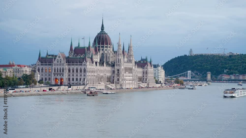 Hungarian Parliament in Budapest at sunset on cloudy day. Chain Bridge, Gell�rt Hill, Royal Palace in background. Boats gently drifting on the Danube River, capturing the city's charm at sunset. Hungarian Parliament in Budapest at sunset on cloudy day. Chain Bridge, Gell�rt Hill, Royal Palace in background. Boats gently drifting on the Danube River, capturing the city's charm at sunset.