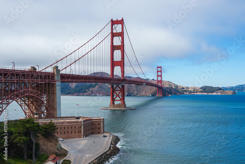 The Golden Gate Bridge spans San Francisco Bay with Fort Point at its base. The International Orange bridge contrasts with blue water and Marin hills. photo