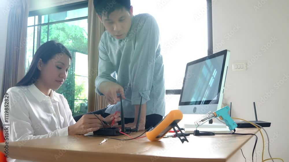 A man and a woman are working on a project together. The woman is holding a tool and the man is looking at a computer monitor. Scene is collaborative and focused A man and a woman are working on a project together. The woman is holding a tool and the man is looking at a computer monitor. Scene is collaborative and focused