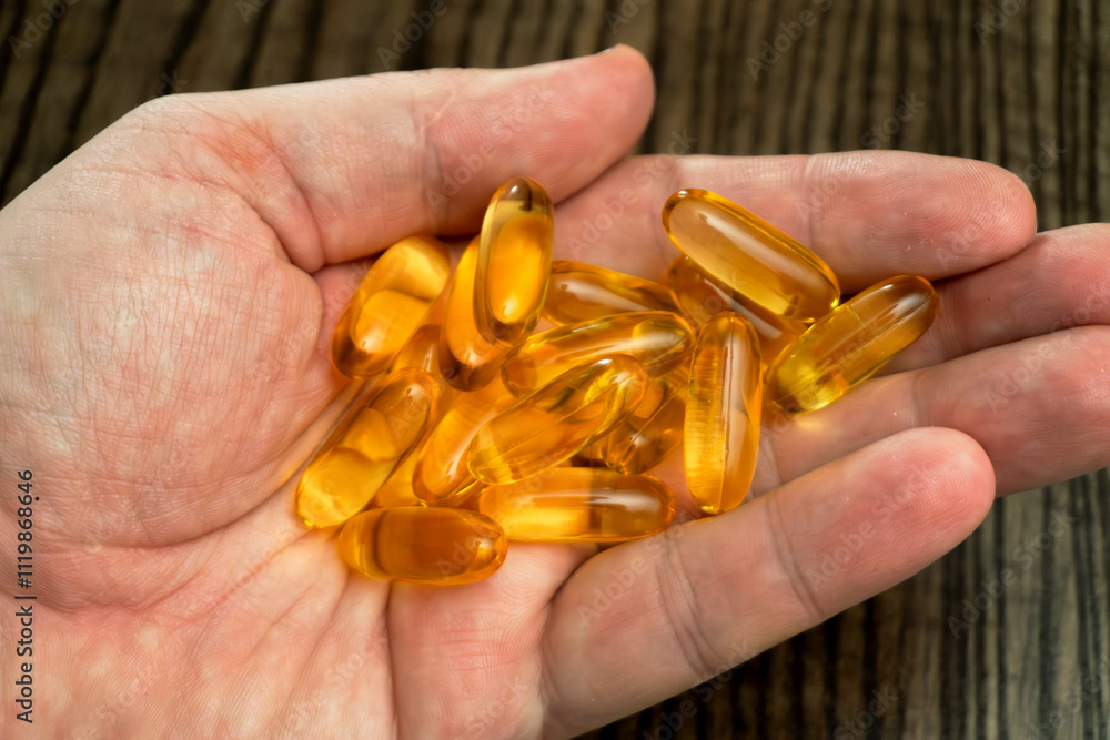 Hand holding multiple golden capsules on wooden surface Hand holding multiple golden capsules on wooden surface