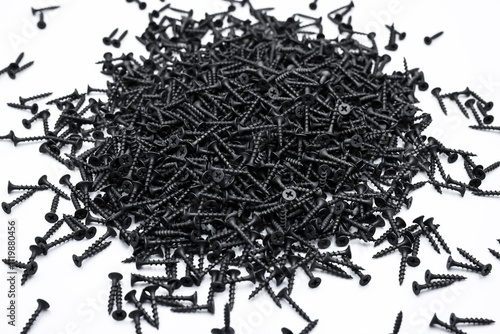 A small pile of black screws on a white background. Fastening materials for fastening drywall structures