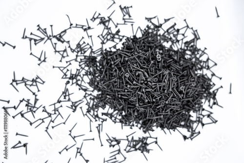 A small pile of black screws on a white background. Fastening materials for fastening drywall structures