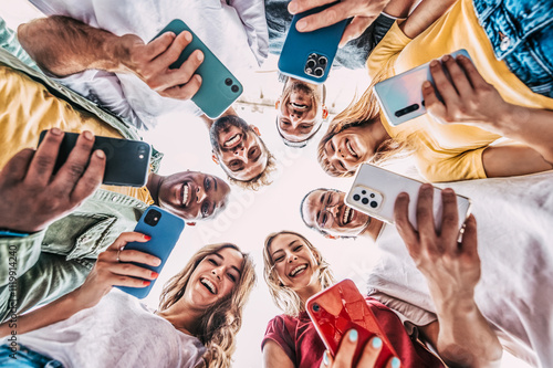 Group of multiracial young people using smart mobile phone device outside - Happy best friends laughing at camera - Trendy technology concept with guys and girls playing video games app on phone photo