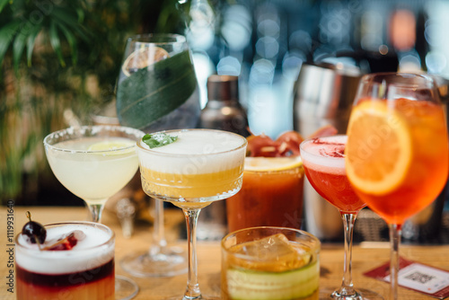 Assorted colorful cocktails close-up in elegant glassware, garnished with fruits and herbs, captured with a shallow depth of field for bokeh effect. Bright indoor bar setting with blurred background