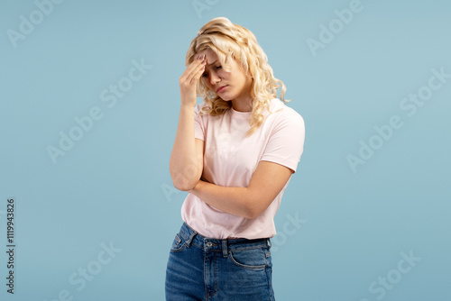 Portrait of sad, upset teenager having headaches, bad news, standing isolated on blue background photo