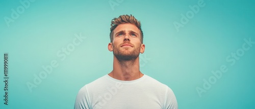 Portrait of a thoughtful man gazing upwards against a turquoise backdrop. photo