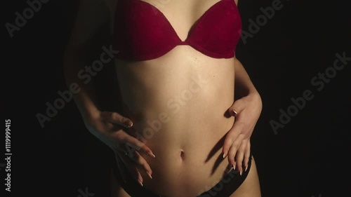 Attractive teenage girl in red bra softly moving her long-nails hands upon her smooth skin in a sensual environment and black background