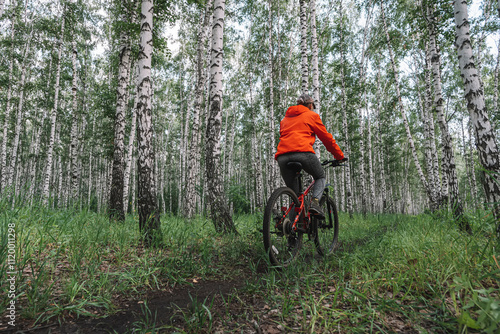 girl on a bike. beautiful wonam in a bright orange jacket on a bike in the forest photo