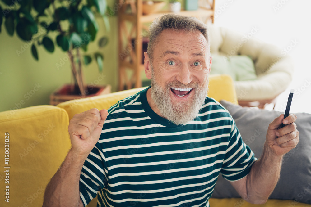 Cheerful senior bearded man relaxing at home with a smile in a striped t-shirt, enjoying leisure time in his cozy living room. Cheerful senior bearded man relaxing at home with a smile in a striped t-shirt, enjoying leisure time in his cozy living room.