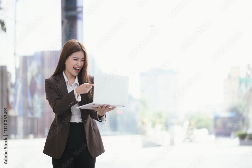 A casually dressed Asian businesswoman sips coffee while playing with her mobile phone outdoors. She smiles confidently and represents the new generation of entrepreneurs.