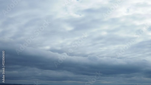 A low, long, heavy, oblong cloud floats across the sky above the lake. Lighter white and gray clouds fly above it. The two layers of clouds fly at different speeds and in different directions. photo