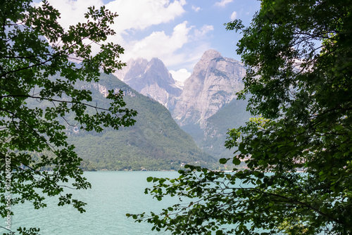 Tree branches framing majestic mountain peak Croz Dell'Altissimo in pristine Brenta Dolomites, National Park Adamello Brenta, Trentino, Italy. Wanderlust at calm alpine lake Lago di Molveno in summer photo