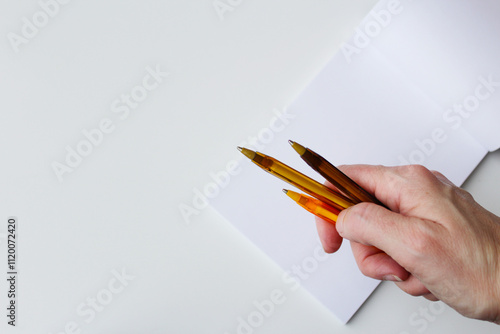 Caucasian hand holding three golden ballpens over a blank paper page. Authorship, handwriting, creative stationery, back to school concept. Copy space available.