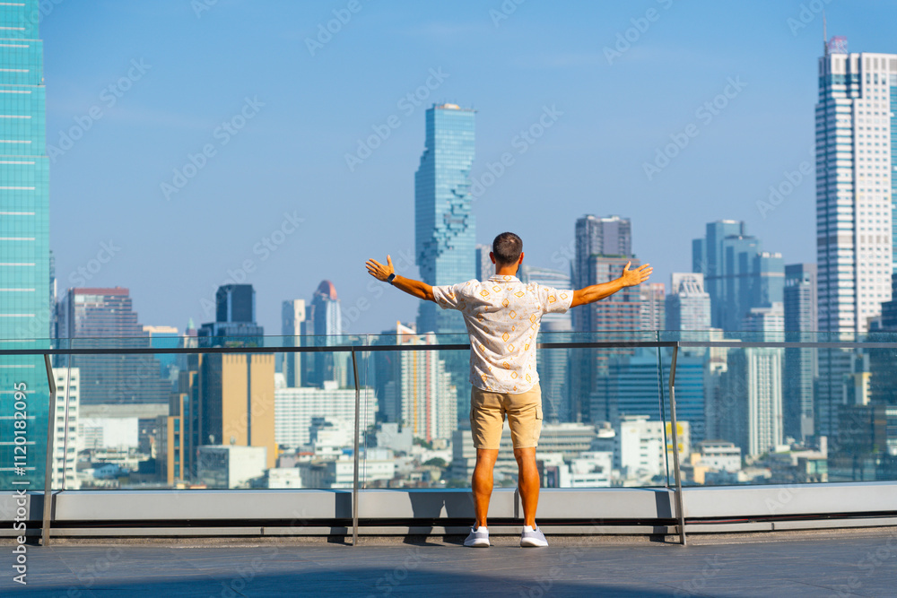 Guy stands with his back raised his hands up high looking at the background of the cityscape view of Bangkok Thailand, concept of opening the exploration of new things in Asia Guy stands with his back raised his hands up high looking at the background of the cityscape view of Bangkok Thailand, concept of opening the exploration of new things in Asia