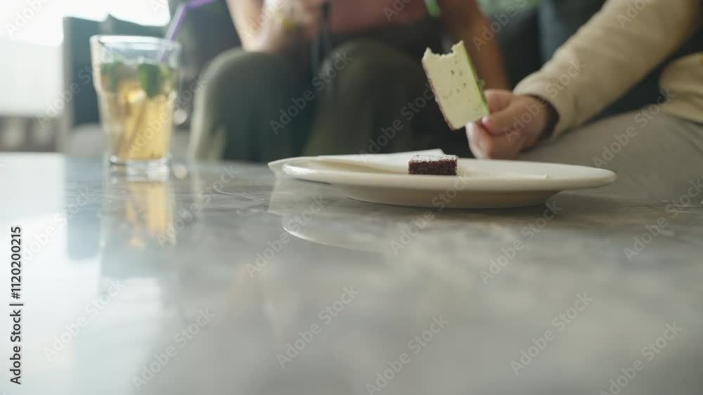 A child takes a bite of cake from a white plate on a marble table, with iced drinks nearby, creating a casual and cozy dining moment in soft lighting. A child takes a bite of cake from a white plate on a marble table, with iced drinks nearby, creating a casual and cozy dining moment in soft lighting.
