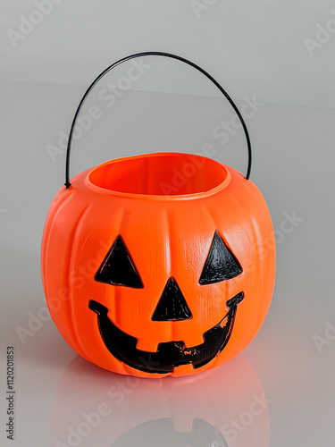 Bright orange plastic pumpkin bucket with a Jack-o'-lantern face and handle. Great for Halloween decor, candy collection, and festive themes.