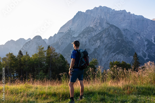 Hiker man with sunrise view of stunning mountain peak Jof Fuart bathed in soft glow of twilight. Massive rugged ridges of majestic Julian Alps in Val Saisera, Valbruna, Friuli Venezia Giulia, Italy photo