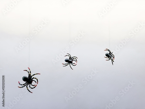 Foto Minimalist Halloween decor with plastic spiders suspended on invisible threads against a white backdrop