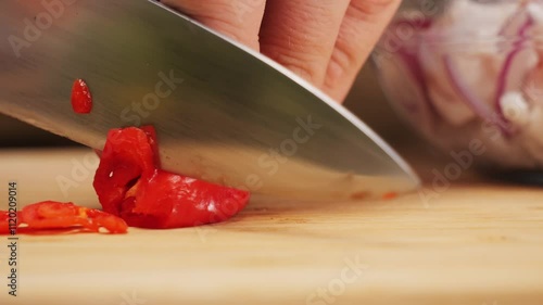 Close-up chopping red hot chilli peppers with sharp knife on cutting board, juicy fresh red hot chilli pepper photo